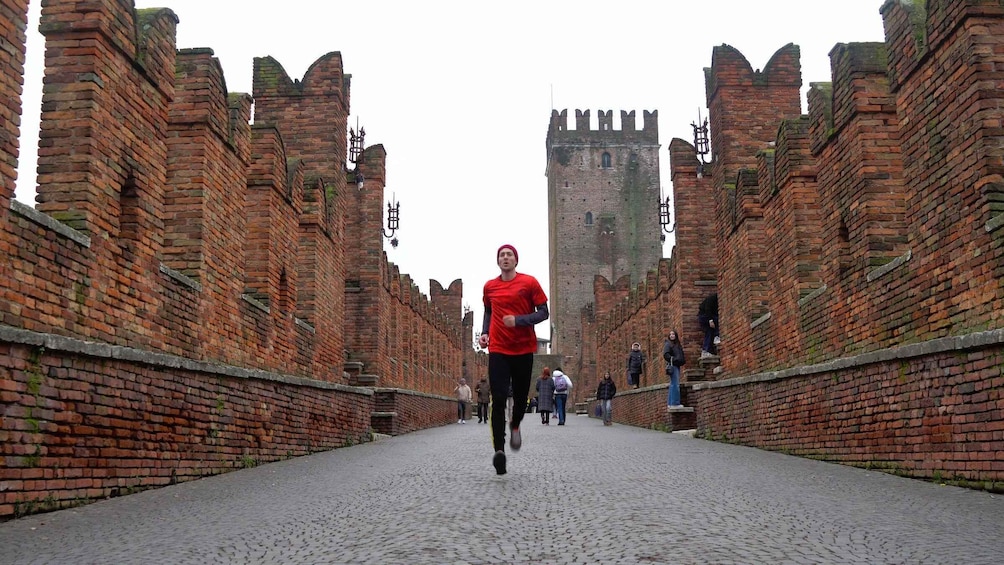 A person running on a cobblestone path flanked by brick walls and a tower. 3