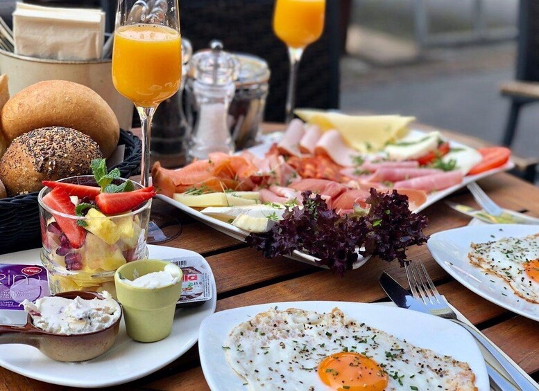A breakfast setting with a plate of smoked salmon, cheese, and vegetables, a glass of orange juice, and a bowl of fruit salad. 5