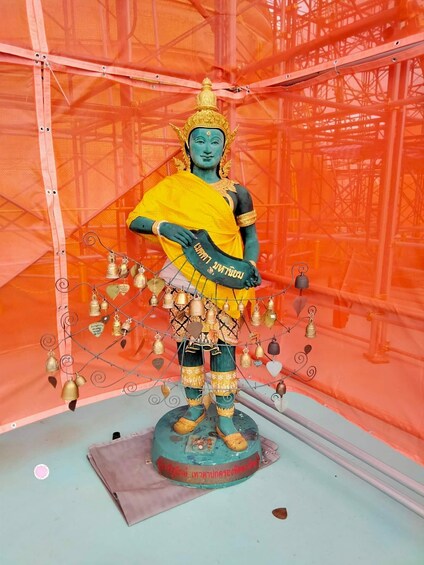 A statue of a deity with a yellow robe and a golden crown, surrounded by hanging bells and a sign with text. 1