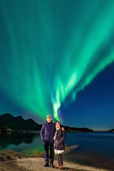 Two people standing by a lake with the aurora borealis in the background. 3