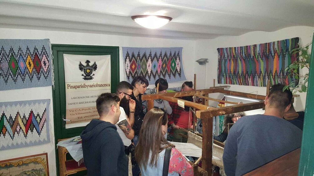 A group of people engaged in textile weaving, with patterned fabrics hanging on the walls. 1