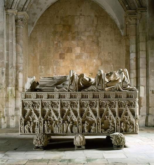 A stone sarcophagus with intricate carvings and figures, set against a stone wall in a historical building. 4