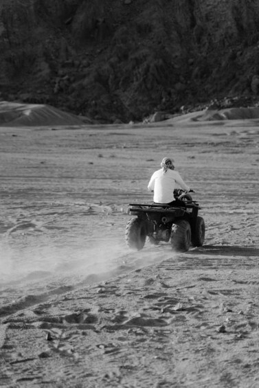 A person riding an ATV on a sandy terrain with a rocky background. 3