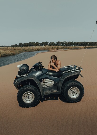 A person sitting on a black Honda ATV on a sandy beach with a river in the background. 4