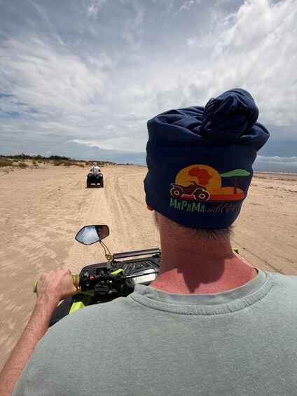 A person riding a quad bike on a sandy path with a cloudy sky in the background. 2
