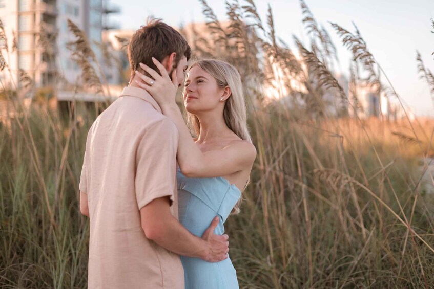 A couple embracing in a field with tall grasses and buildings in the background. 5
