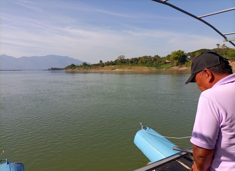 A man on a boat with a calm river, distant mountains, and a green shoreline. 5