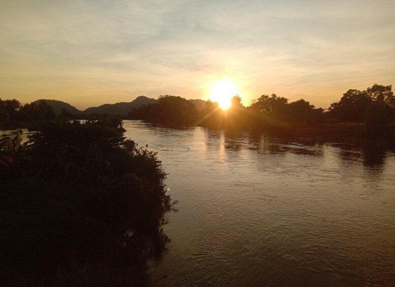 A river at sunset with the sun low on the horizon, surrounded by trees and hills. 1