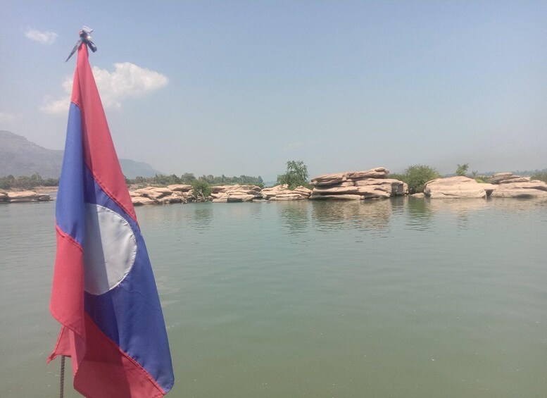 A flagpole with a flag, a calm river, and rocky outcrops in the background. 4