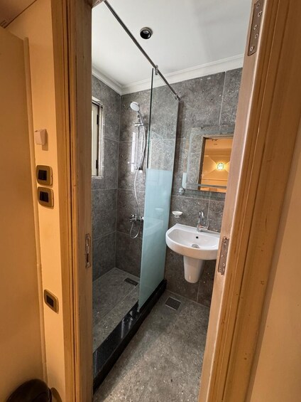 A bathroom with a glass-enclosed shower, a white sink, and marble walls. 4