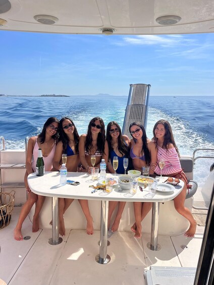 A group of people on a boat with a table set for a meal and drinks, surrounded by water and a clear sky. 4