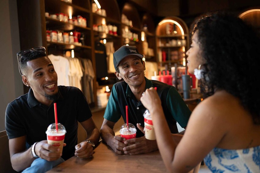 Three people sitting at a table with drinks, in a cafe with shelves of bottles in the background. 2