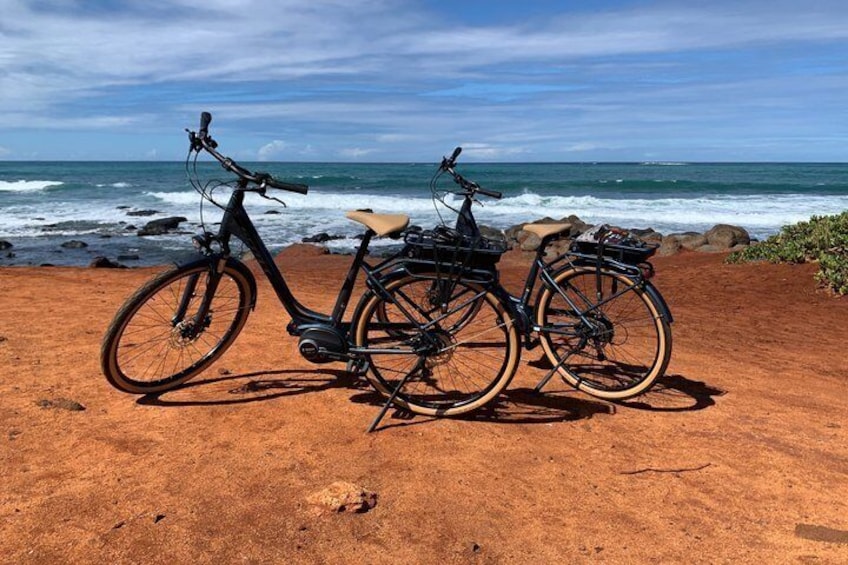 Two bicycles parked on a sandy beach with the ocean in the background. 1