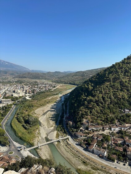 A river winding through a valley with a bridge, surrounded by hills and a town. 4