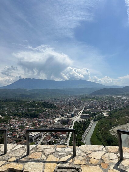 A stone-paved viewing platform overlooking a city with a river, mountains, and a clear sky. 3