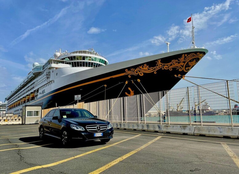 A cruise ship docked at a port with a black Mercedes-Benz car in the foreground. 2