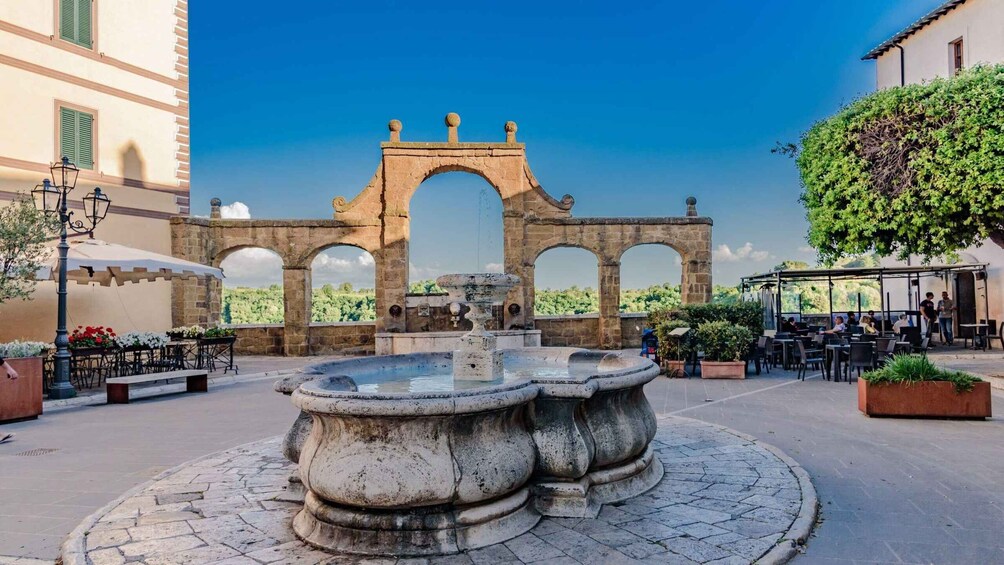 A historic stone archway, a central fountain, and outdoor seating areas in a courtyard. 5