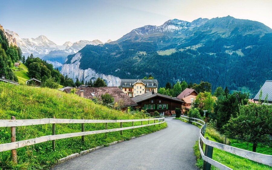 A winding road through a mountainous village with traditional houses and a backdrop of snow-capped peaks. 4