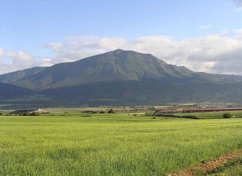 A mountain range with a clear sky, a green field in the foreground, and a red building in the midground. 4