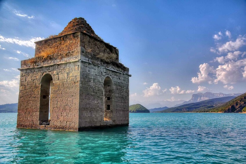 A stone tower in the water with clear skies and distant mountains. 1