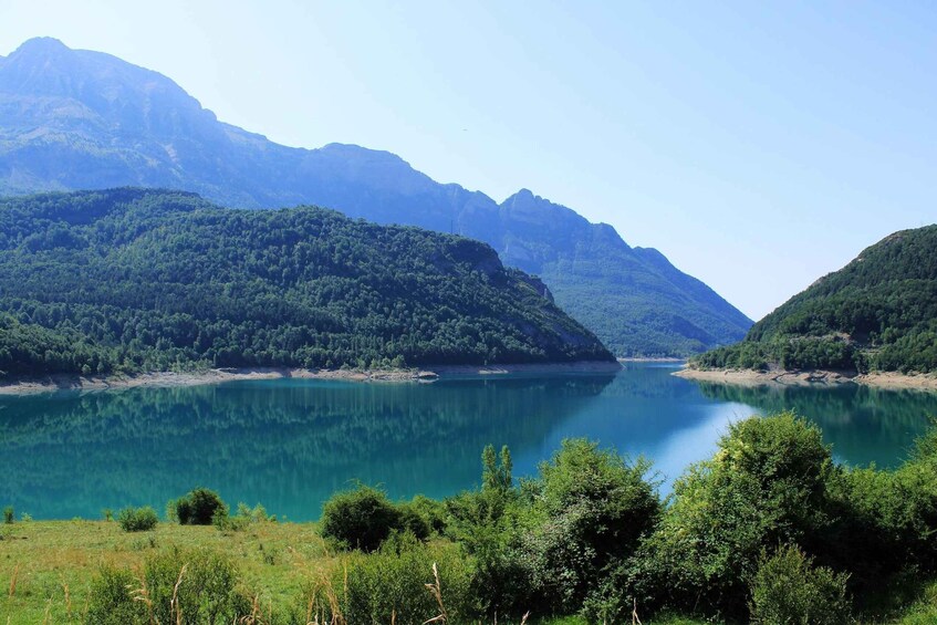 A calm lake surrounded by lush green mountains under a clear sky. 3