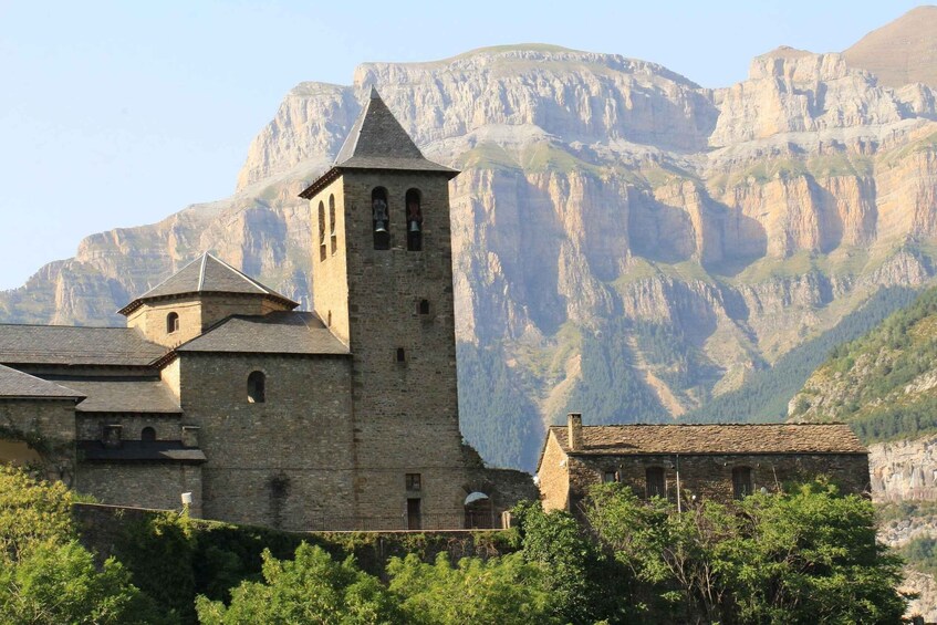 A historic stone church with a bell tower, surrounded by lush greenery and mountains in the background. 5