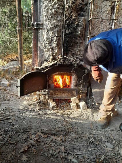 A person opening a wood-fired oven with flames visible inside. 4