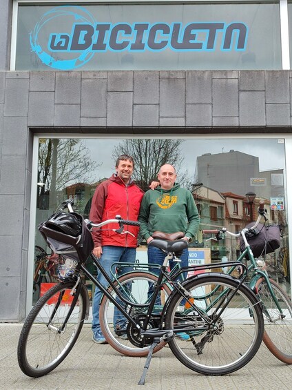 Two men standing in front of a bicycle shop with a bicycle leaning against the window. 3