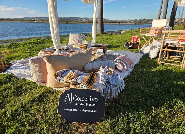 A picnic setup with a sign reading 'AJCollectivo Curated Picnics' by a lakeside. 2
