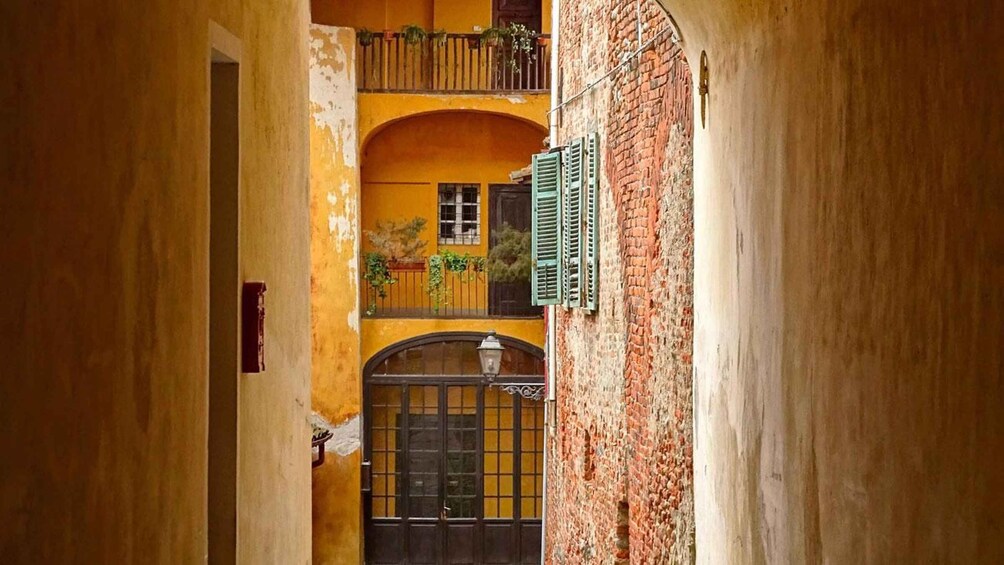 A narrow alleyway with a yellow building, a brick wall, and a window with shutters. 3