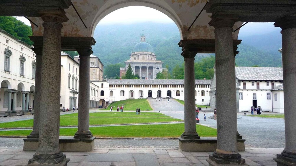 A historical courtyard with columns, a central lawn, and a distant building with a dome. 1