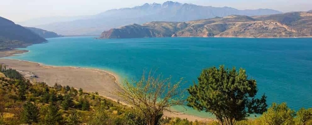 A coastal landscape with a clear turquoise sea, a sandy beach, and surrounding hills. 5