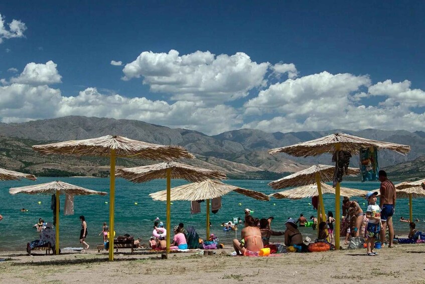 A beach with people sunbathing and swimming, surrounded by mountains and clear blue water. 4