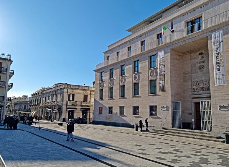 A city square with historic buildings, a clear sky, and people walking. 3