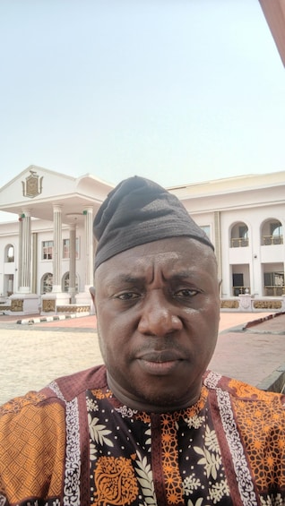 A man in traditional attire standing in front of a building with classical architecture. 1