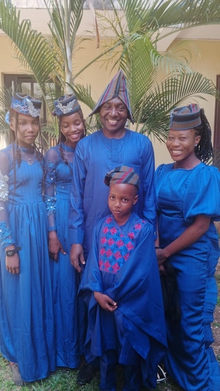 A group of people in blue attire with decorative headpieces, standing outdoors with palm trees in the background. 3