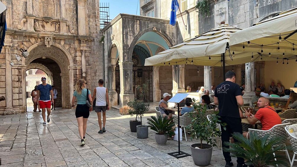 A cobblestone street with stone buildings, outdoor seating, and people walking. 5