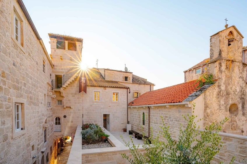 A narrow stone alleyway with buildings on either side, a small garden, and a church tower. 4