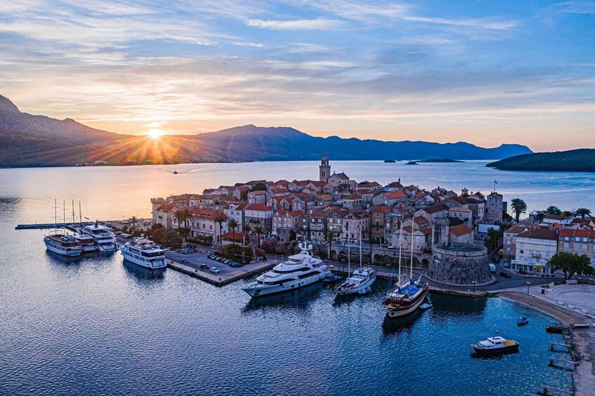 A coastal town with historic buildings, a marina with yachts, and mountains in the background. 1