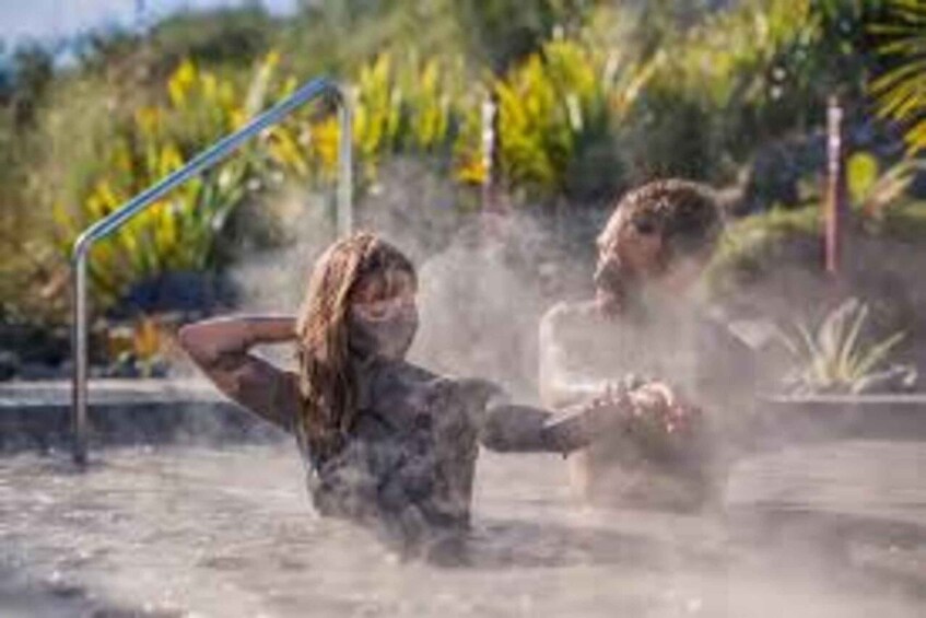 A person in a body of water with steam rising, surrounded by greenery and a metal structure. 3