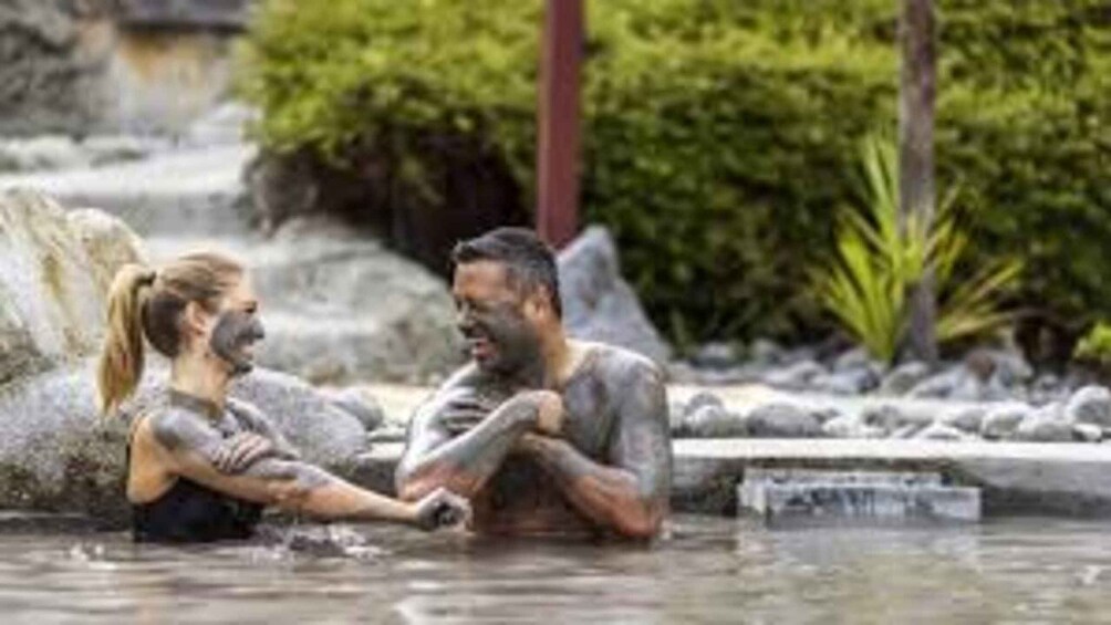 A couple in a natural hot spring setting with water, rocks, and greenery. 4