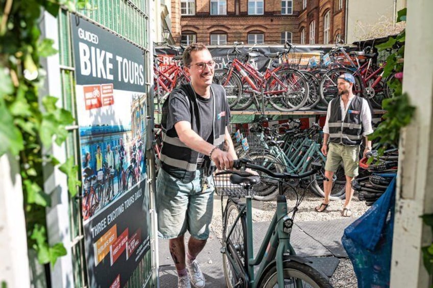 A man on a bicycle, a bike rack with multiple bicycles, and a poster advertising guided bike tours. 1