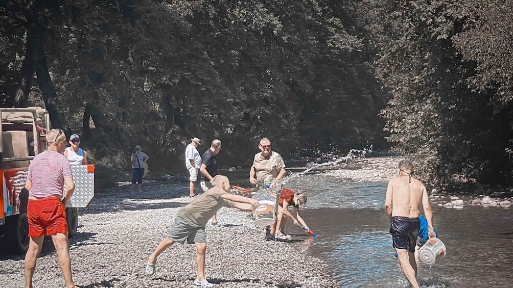 People by a river with a truck and a rocky shore. 2