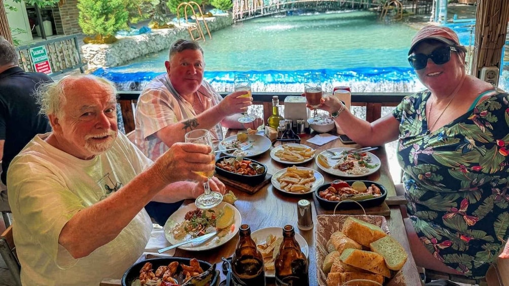 A group of people toasting at a table with various dishes and drinks, overlooking a body of water. 4