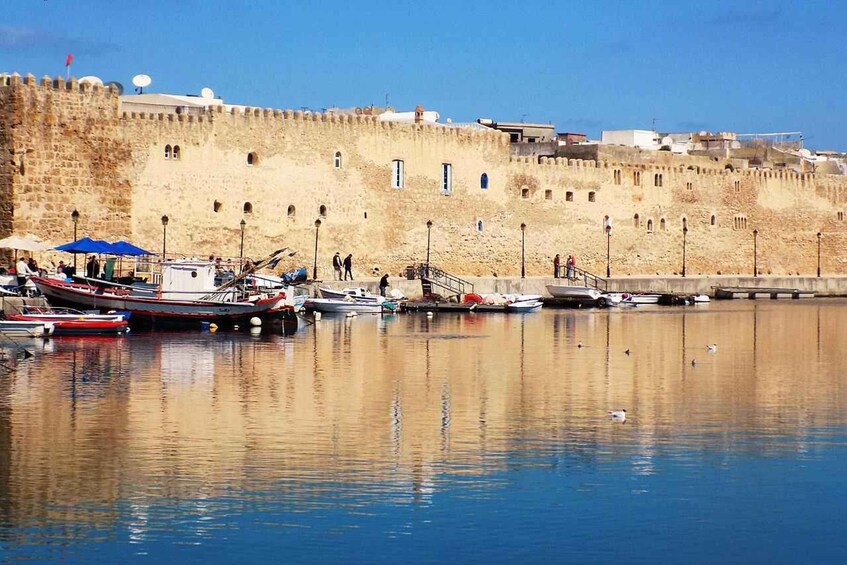 A harbor with boats docked, a stone wall, and a clear sky. 3
