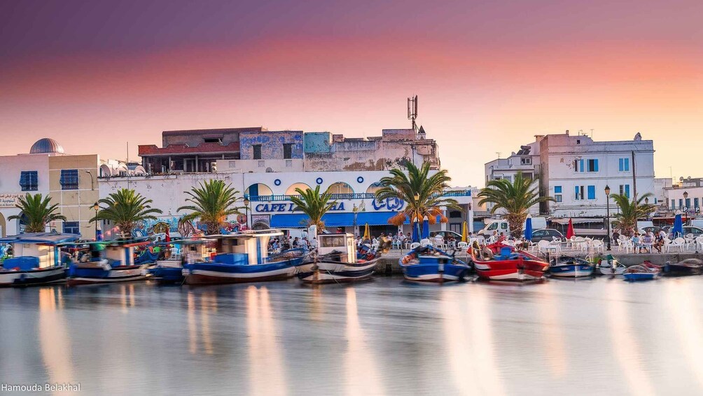 A waterfront with boats docked, palm trees, and buildings with signage. 5