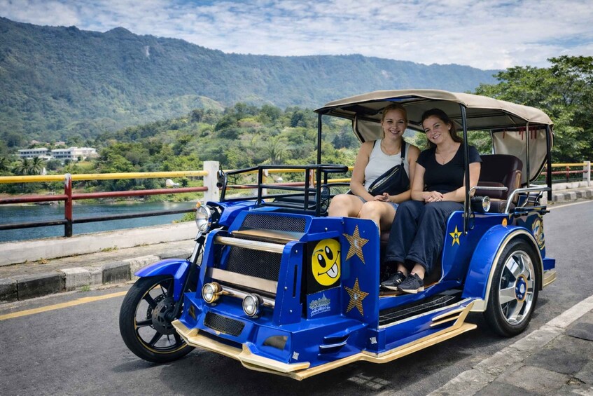 A vintage blue car with a smiling face and stars, driving on a road with a lake and mountains in the background. 5