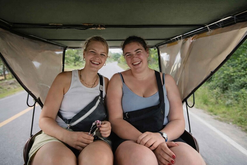 Two people seated in a vehicle with a road and greenery in the background. 4