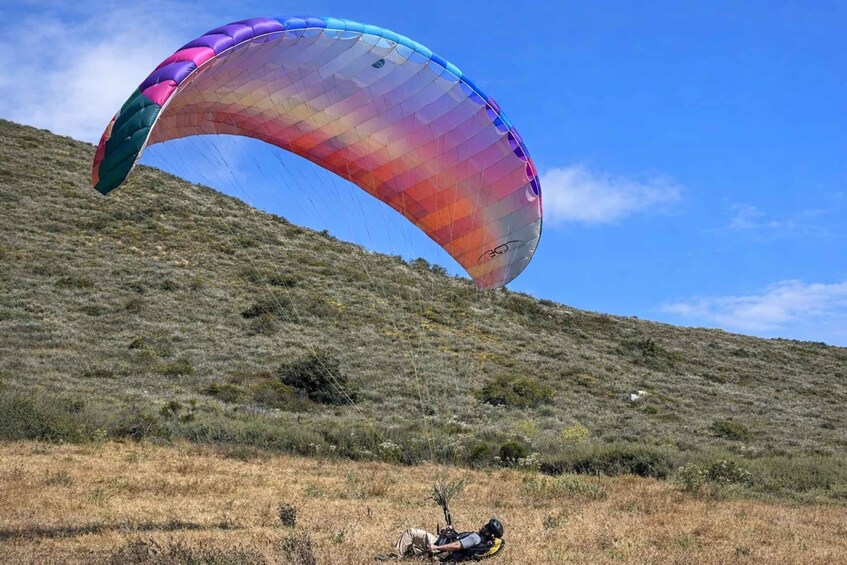 A person paragliding with a colorful canopy over a grassy hill. 3