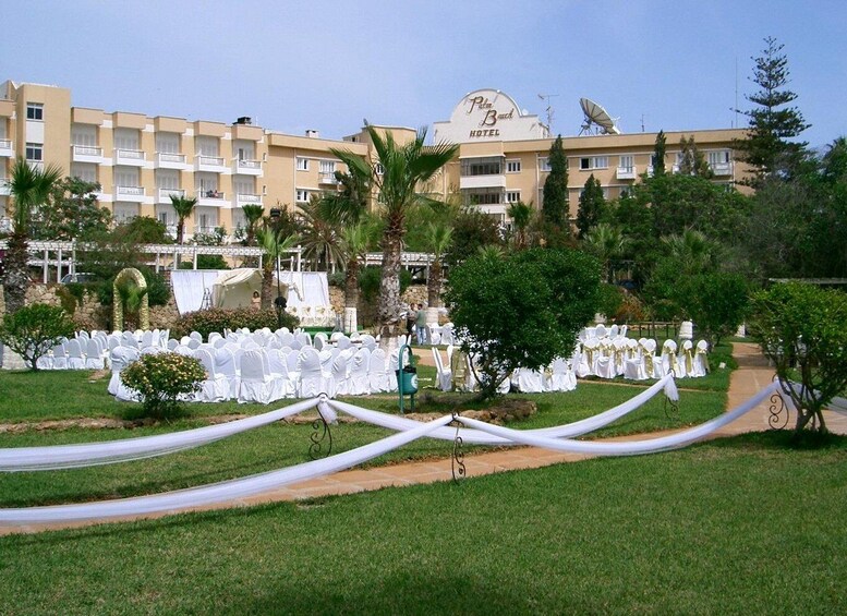 A hotel with a white facade, palm trees, and a white chair-lined pathway. 4
